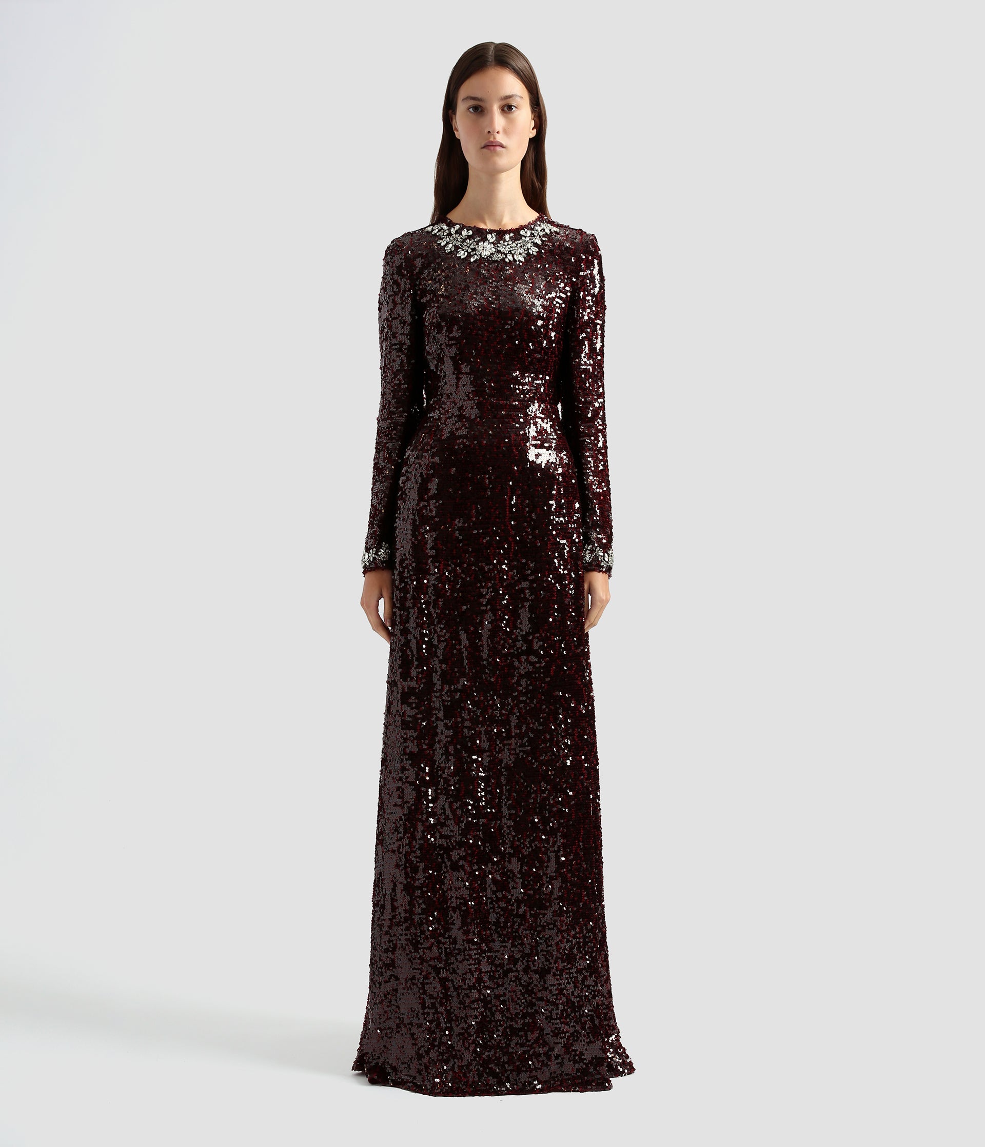 This burgundy sequin gown makes the ultimate statement. Long sleeves and a slim floor length dress in all over sequin with crystal florals around the neck and cuffs. 