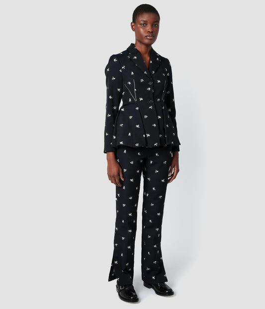 Tailored slim leg trousers for women by designer Erdem. The tailored trousers are crafted from a navy jacquard with white ditsy floral embroidery. The tailored floral trousers are worn with a matching peplum single breasted blazer. 