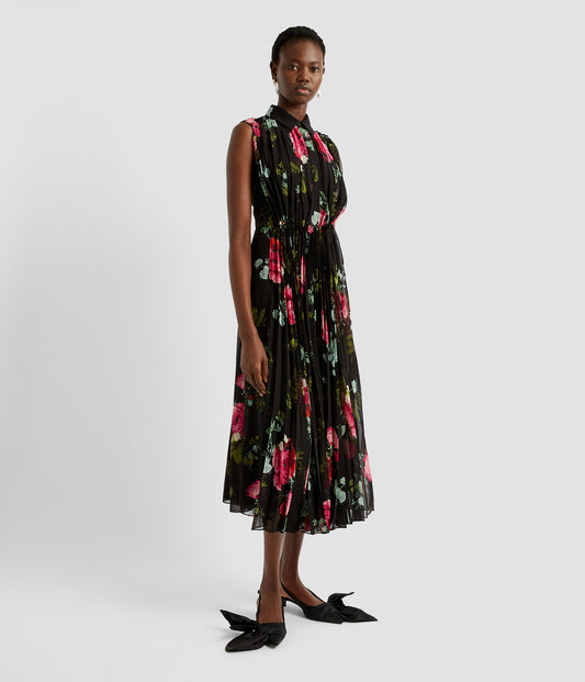 A pleated shirt dress with a pleated sleeveless bodice and pleated midi skirt, which are joined by a gathered waist. The pleated shirt dress is made from a voile thats black with a bright rose print. 