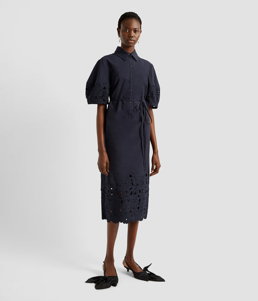 A midi dress with short puff sleeves and tie waist. The short sleeve midi dress is navy with floral cutwork embroidery on the sleeves and hem. The dress has a shirt collar and buttons down the bodice. 