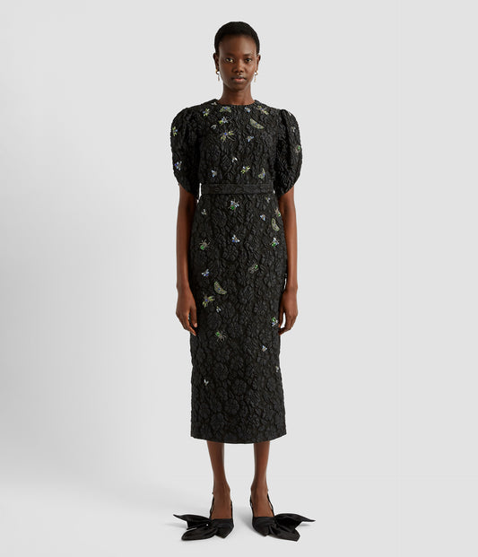 A black crew neck midi dress in floral matelassé with crystal and beeded insect details. The midi dress features a crew neck bodice, pencil skirt and tulip sleeves. 