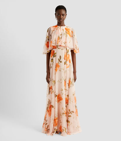 An elegant dress with a cape overlay from designer ERDEM. The floor length dress is crafted in light pink rose print silk voile. It's feminine and striking with the cape addition.