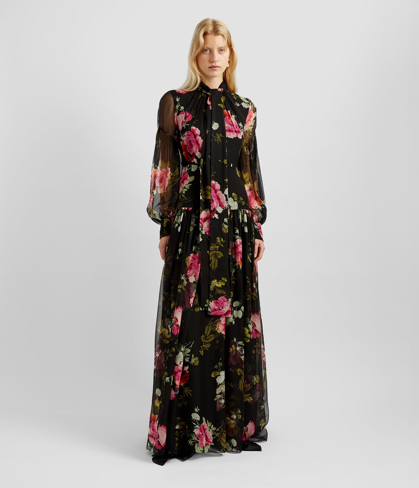 Blouson long dress in black with a pink and red rose print. The blouson long dress has a gathered tie neck, blouson sleeves and a drop waist. 