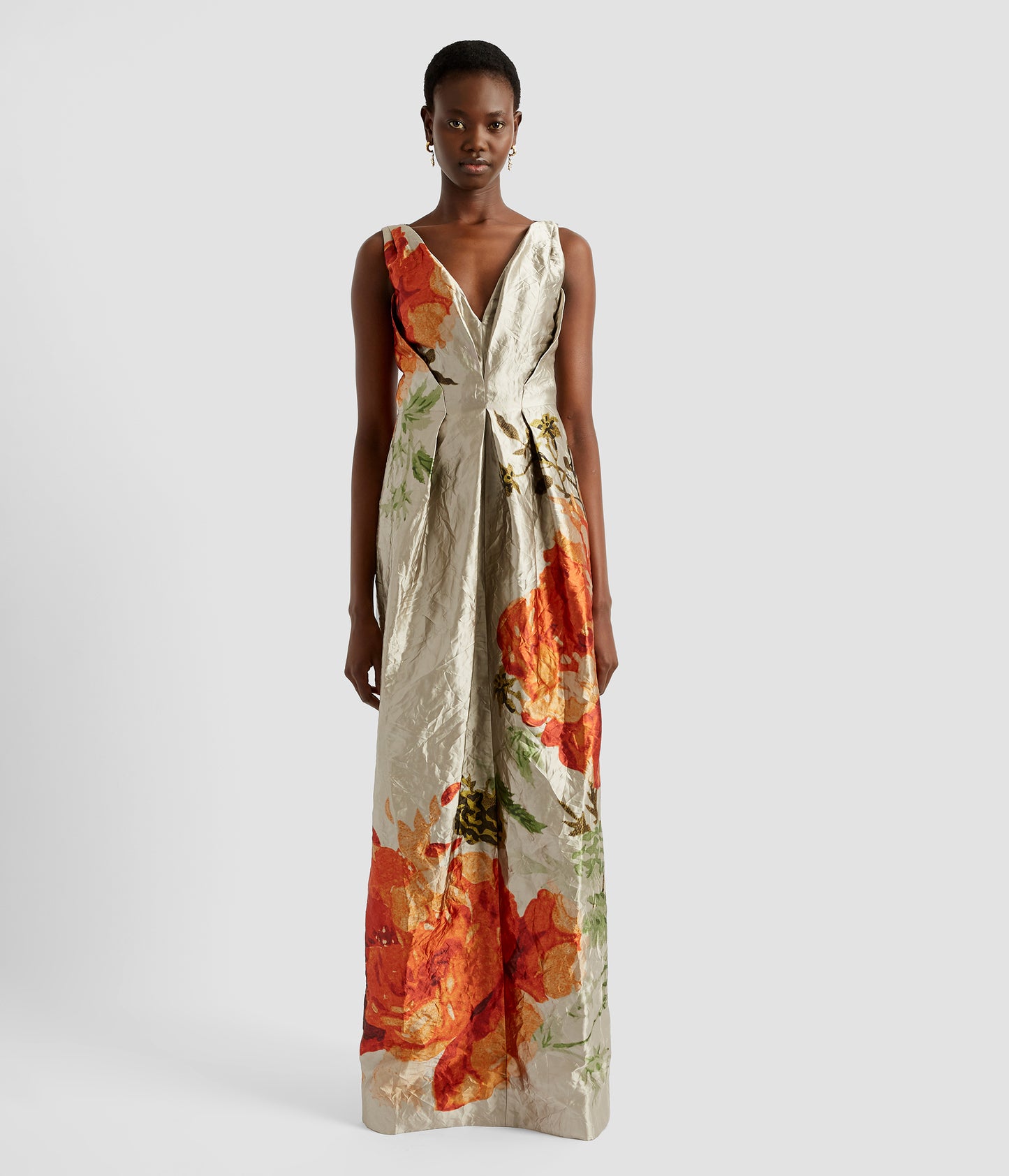 A luxury v neck gown in textured satin by ERDEM. The v neck gown features dramatic pleats at the waist, is sleeveless and has large orange rose motifs. 