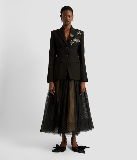 A black single breasted blazer with large crystal embroidered bugs on one shoulder and lapel. The single breasted blazer has a classic cut and is worn with a feminine tulle skirt.  