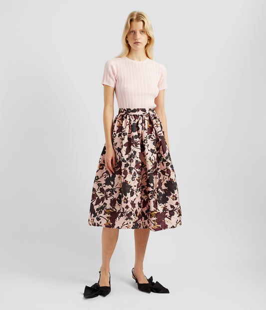 A knitted pointelle t-shirt top in pale pink. The knitted top has a classic crew neck with short t-shirt sleeves. Worn in the image with a floral print flared midi skirt. 