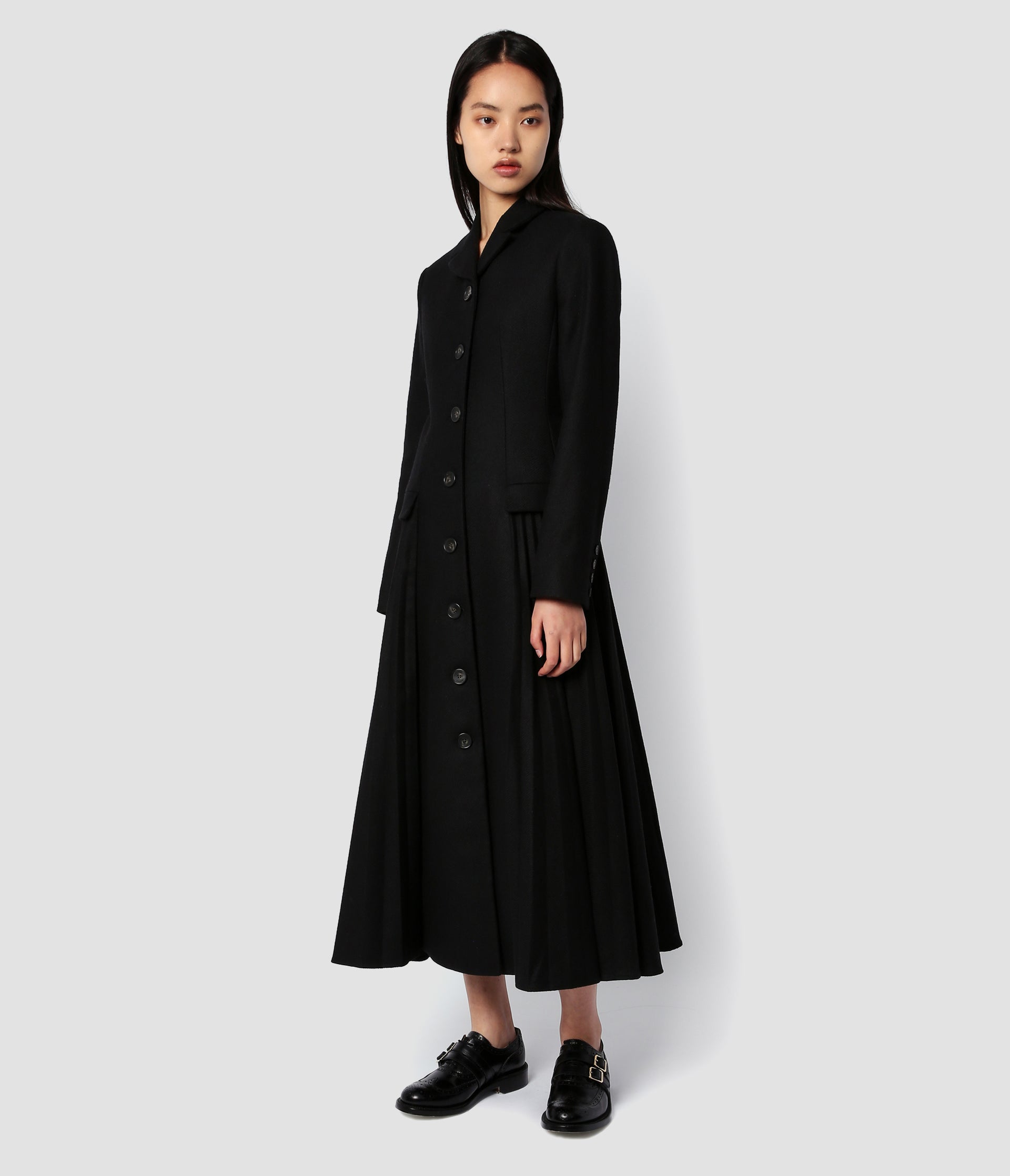 A black single breasted coat by designer Erdem with pleating detail at each side extending from the flap pockets. With a rounded lapel collar an midi length, the coat has all the classic details of a single breasted coat. 