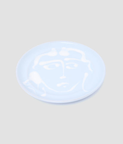 A handmade ceramic plate designed by ERDEM. The plate is sky blue and features a handpainted sketchy face in the design.