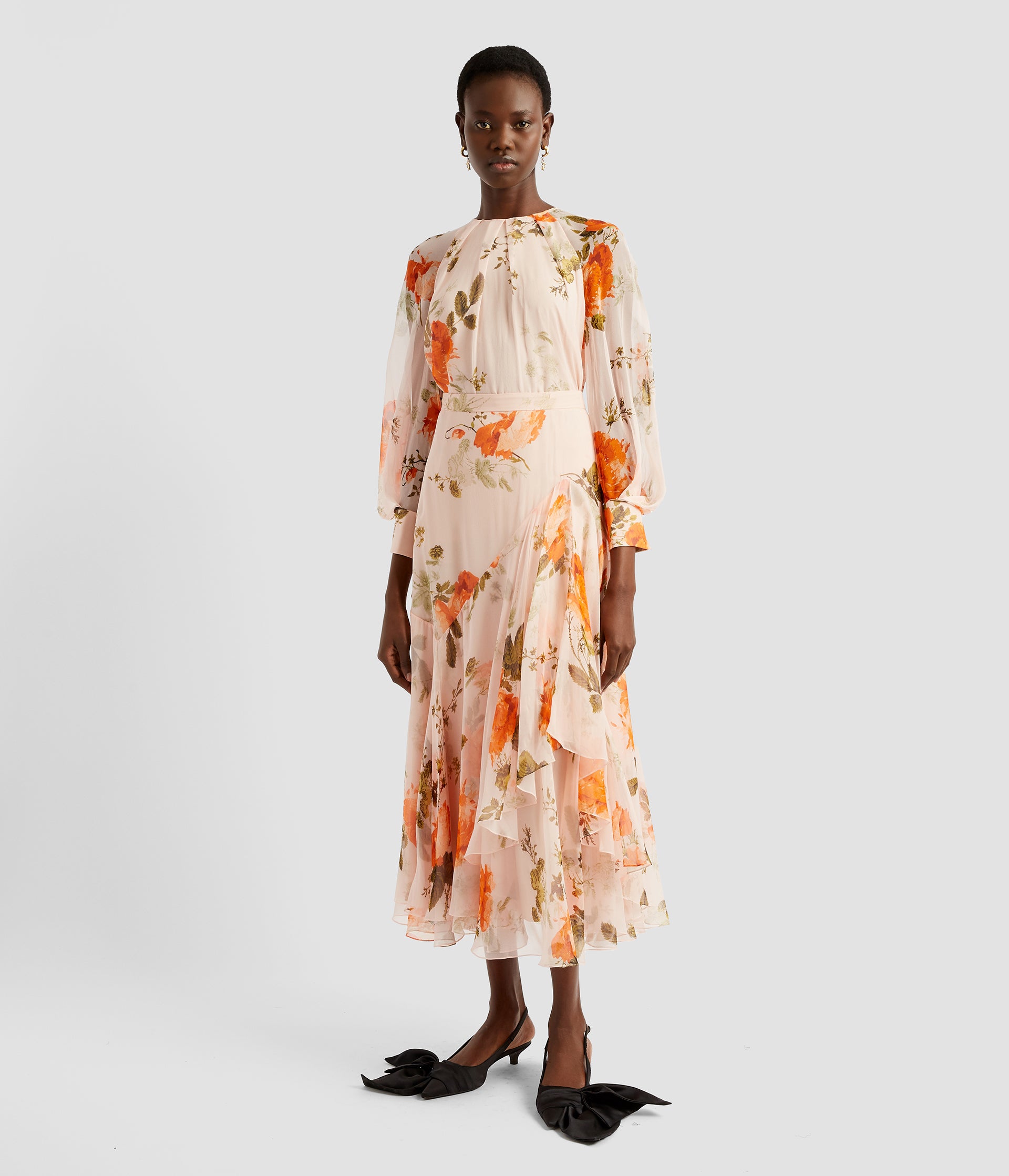 A gathered blouse in pale pink with Rose print in orange. With long blouson sleeves this gathered blouse is made from silk voile and worn with a matching midi skirt. 