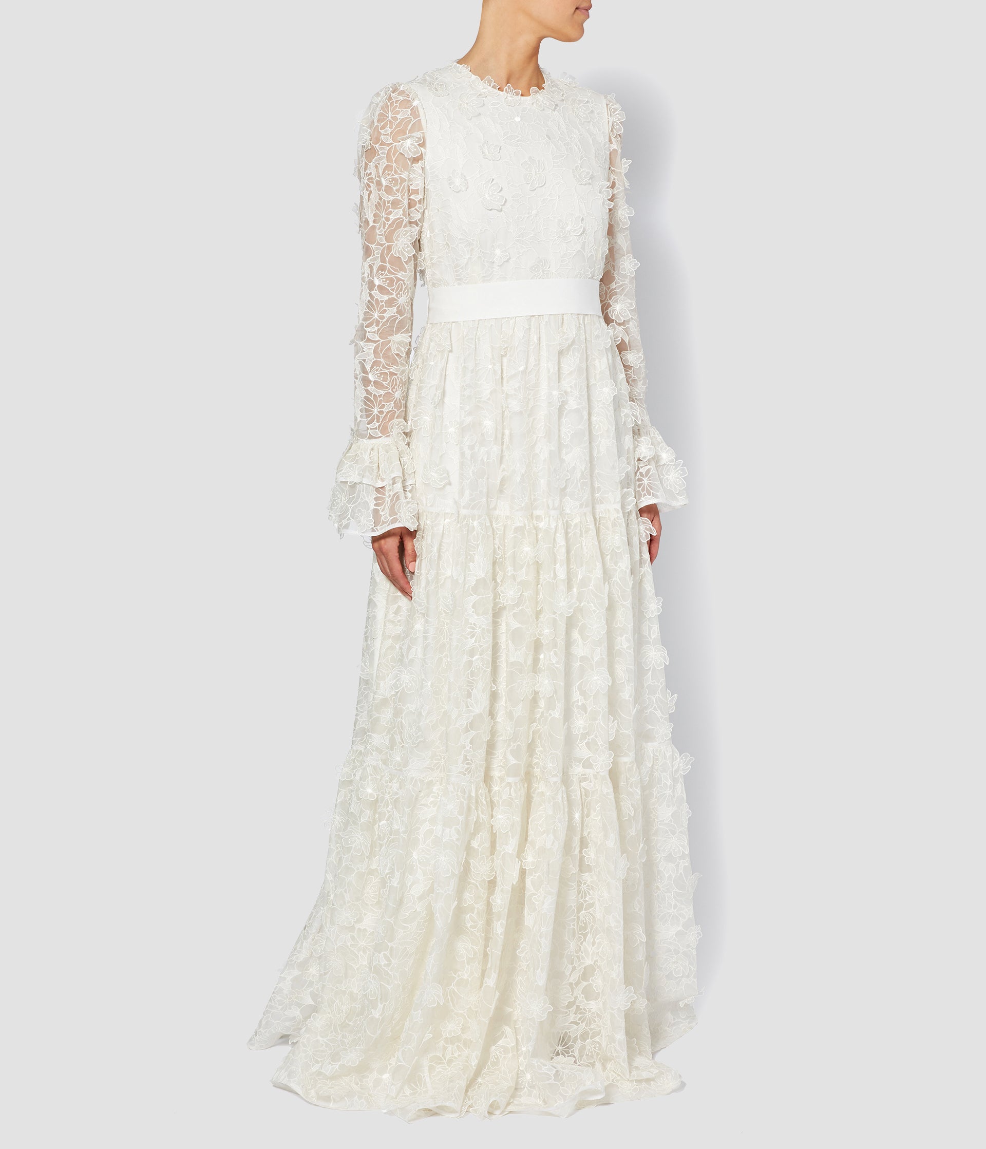 An organza wedding gown in ivory with a floor length skirt and long sleeves. The organza dress features ruffled cuffs and a 3D flower texture. 