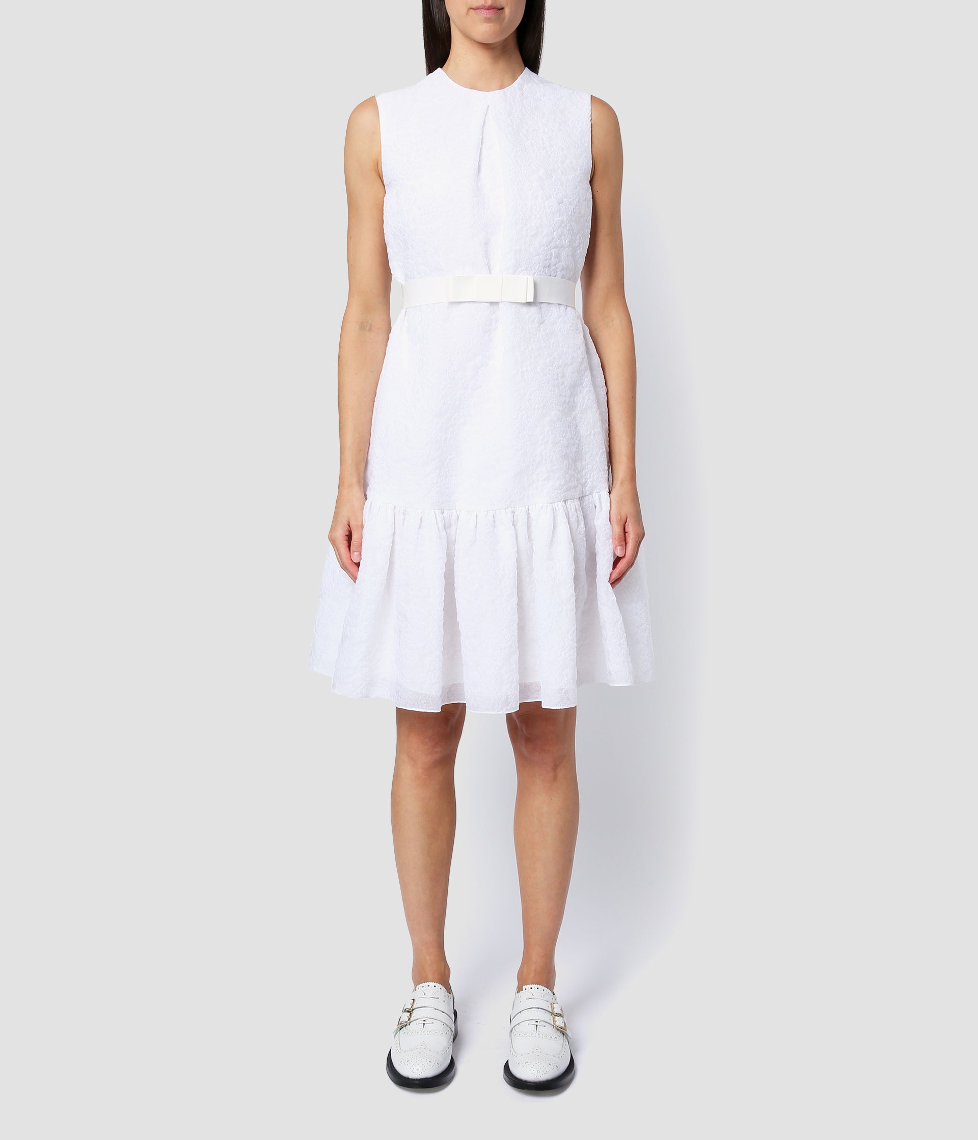 Maple dress by designer Erdem. The sleeveless short dress features a bow waist belt and a gathered tiered skirt. Made from white organza cloque suitable for a short wedding dress.