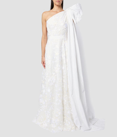 Asymmetric one-shoulder wedding dress with a large bow on the shoulder. The wedding dress is made from ivory organza with embroidered flowers that is fitted at the waist with a flared skirt.